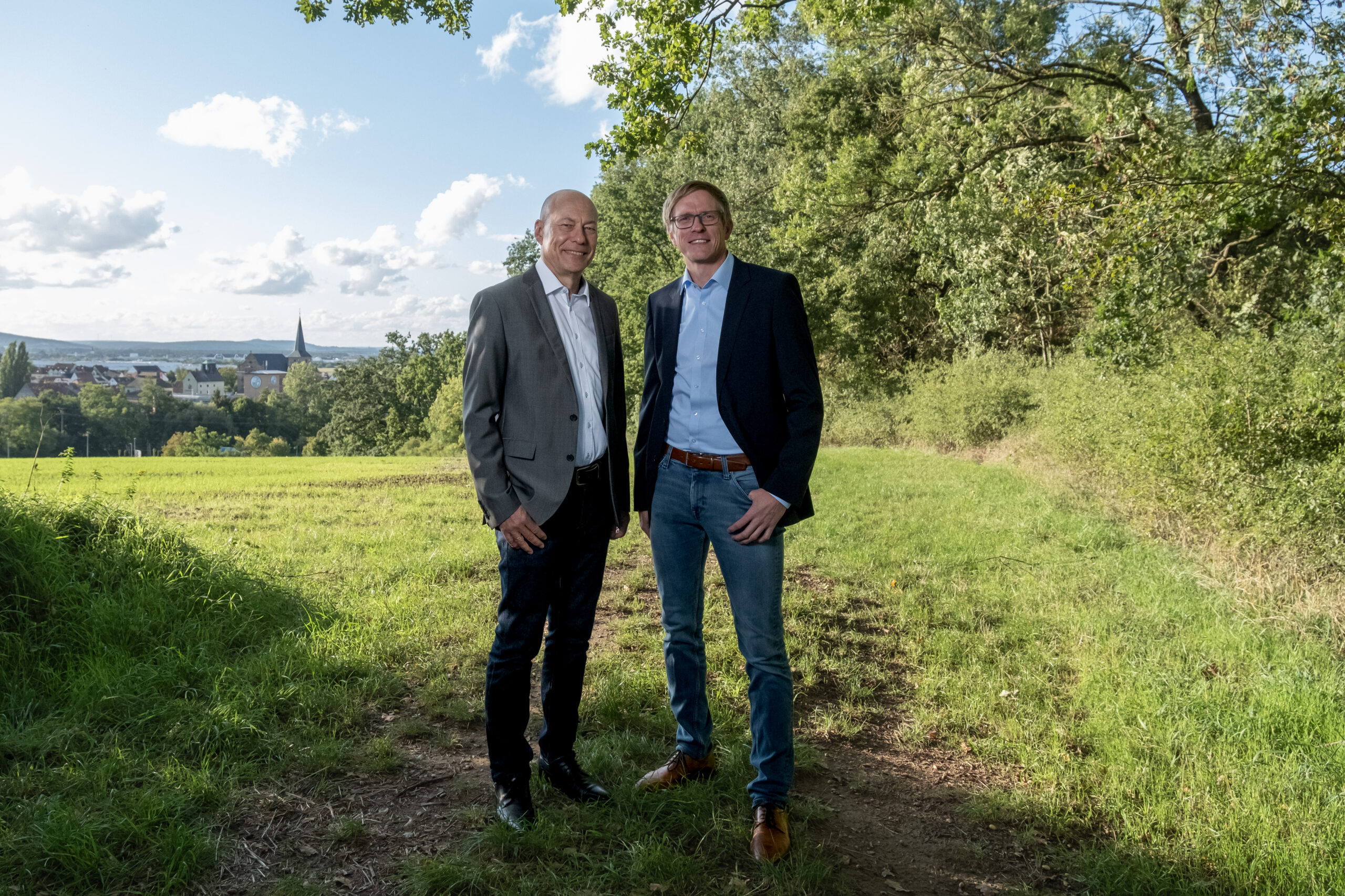 A woman wearing glasses, a white blouse, and a tan corduroy blazer sits at a table with her hands clasped during a professional meeting